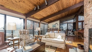 A spacious living area with a wooden ceiling, large windows, a sofa, a coffee table, and a fireplace. - Spend your vacation at this relaxing waterfront retreat on Green Hill Pond. (South Kingstown)