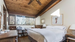 A bedroom with a large bed, wooden ceiling, bookshelves, a desk, and a window with a view of trees. - Spend your vacation at this relaxing waterfront retreat on Green Hill Pond. (South Kingstown)