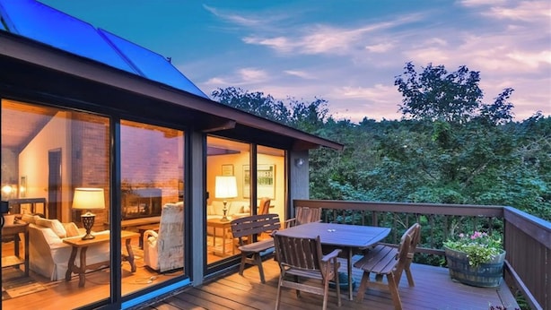 A wooden deck with a dining table and chairs, a sofa, and a lamp. - Spend your vacation at this relaxing waterfront retreat on Green Hill Pond. (South Kingstown)
