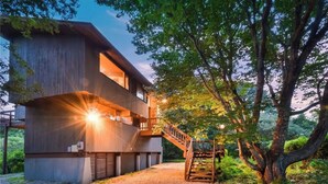 A modern two-story building with a wooden exterior, a staircase leading to a balcony, and a tree in the foreground. - Spend your vacation at this relaxing waterfront retreat on Green Hill Pond. (South Kingstown)