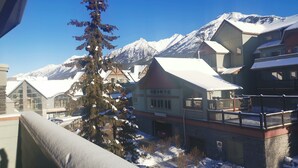 A snow-covered mountain town with buildings featuring traditional architecture and a prominent evergreen tree in the foreground. - Close To It All! Rocky Mountain 2BR Loft Penthouse - Resort w Pool & 3 Hot Tubs! (Canmore)