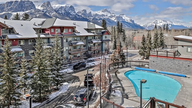 A resort with a pool, snow-covered trees, and mountains in the background. - Close To It All! Rocky Mountain 2BR Loft Penthouse - Resort w Pool & 3 Hot Tubs! (Canmore)