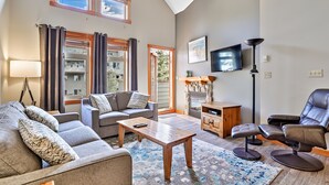 A living room with a sofa, a coffee table, a fireplace, a TV, and a massage chair. - Close To It All! Rocky Mountain 2BR Loft Penthouse - Resort w Pool & 3 Hot Tubs! (Canmore)