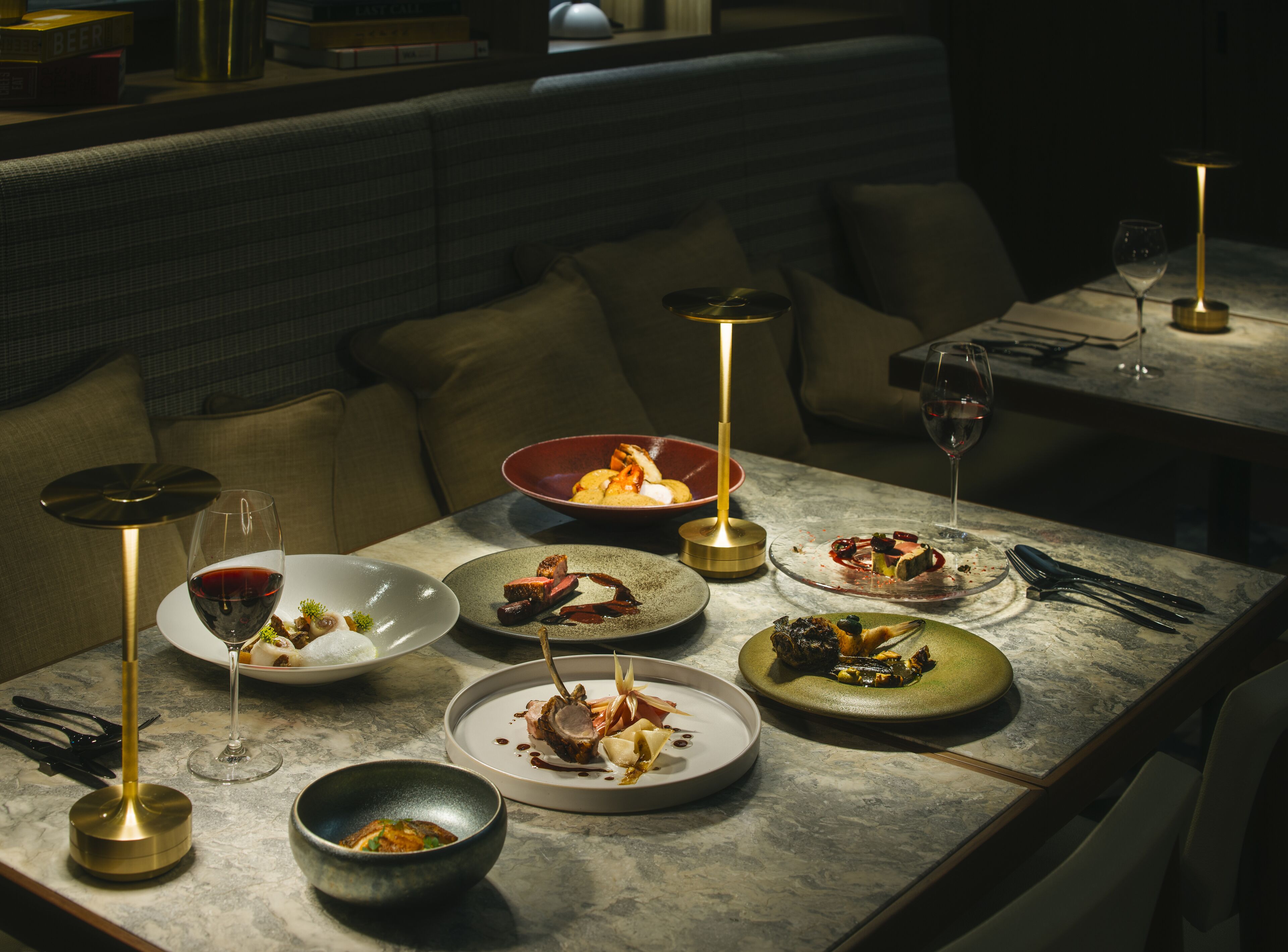 A dimly lit restaurant with a marble table set for a meal, featuring various dishes and wine glasses.