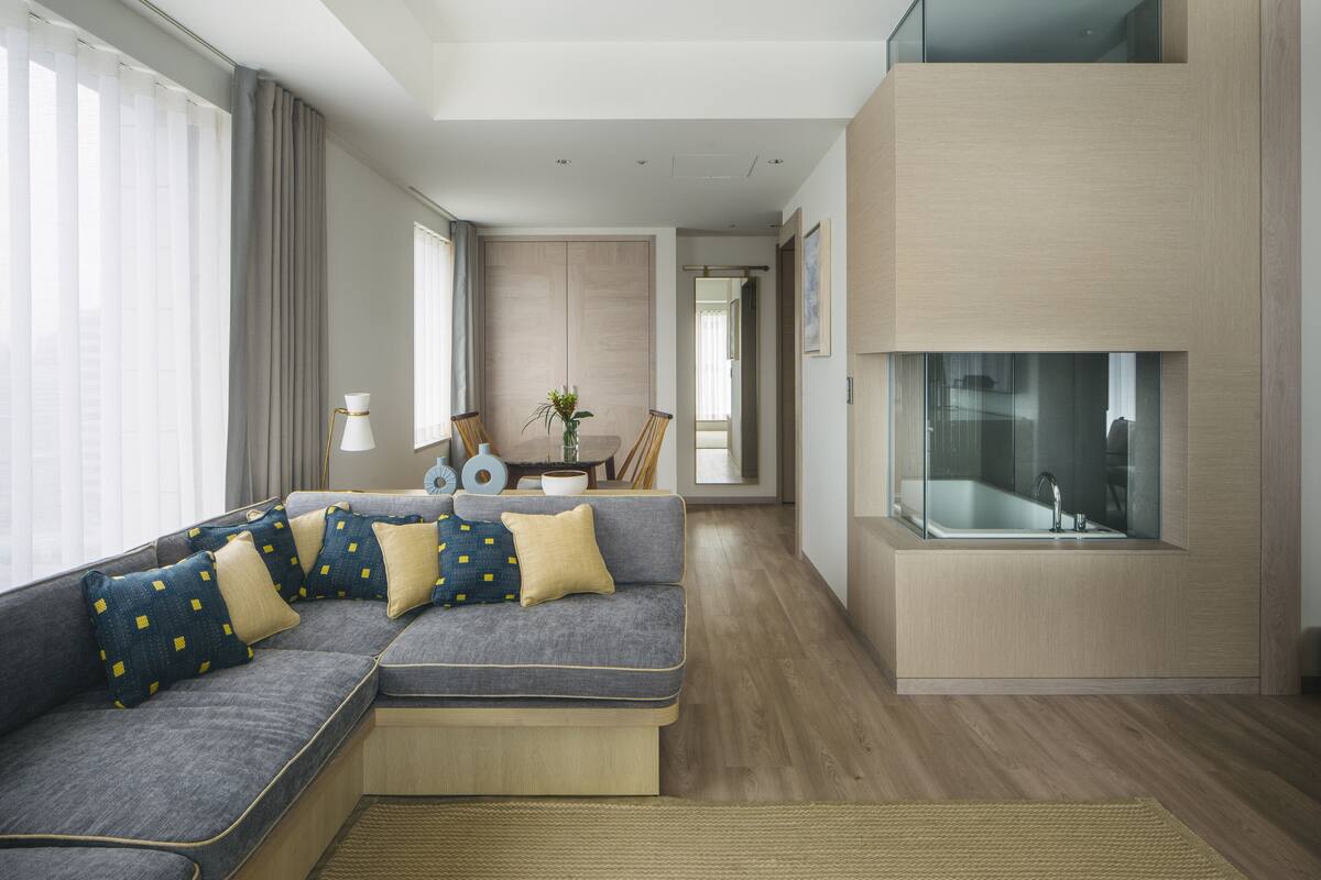 A modern living room with a sectional sofa, a glass-enclosed fireplace, and a view of the city through large windows.