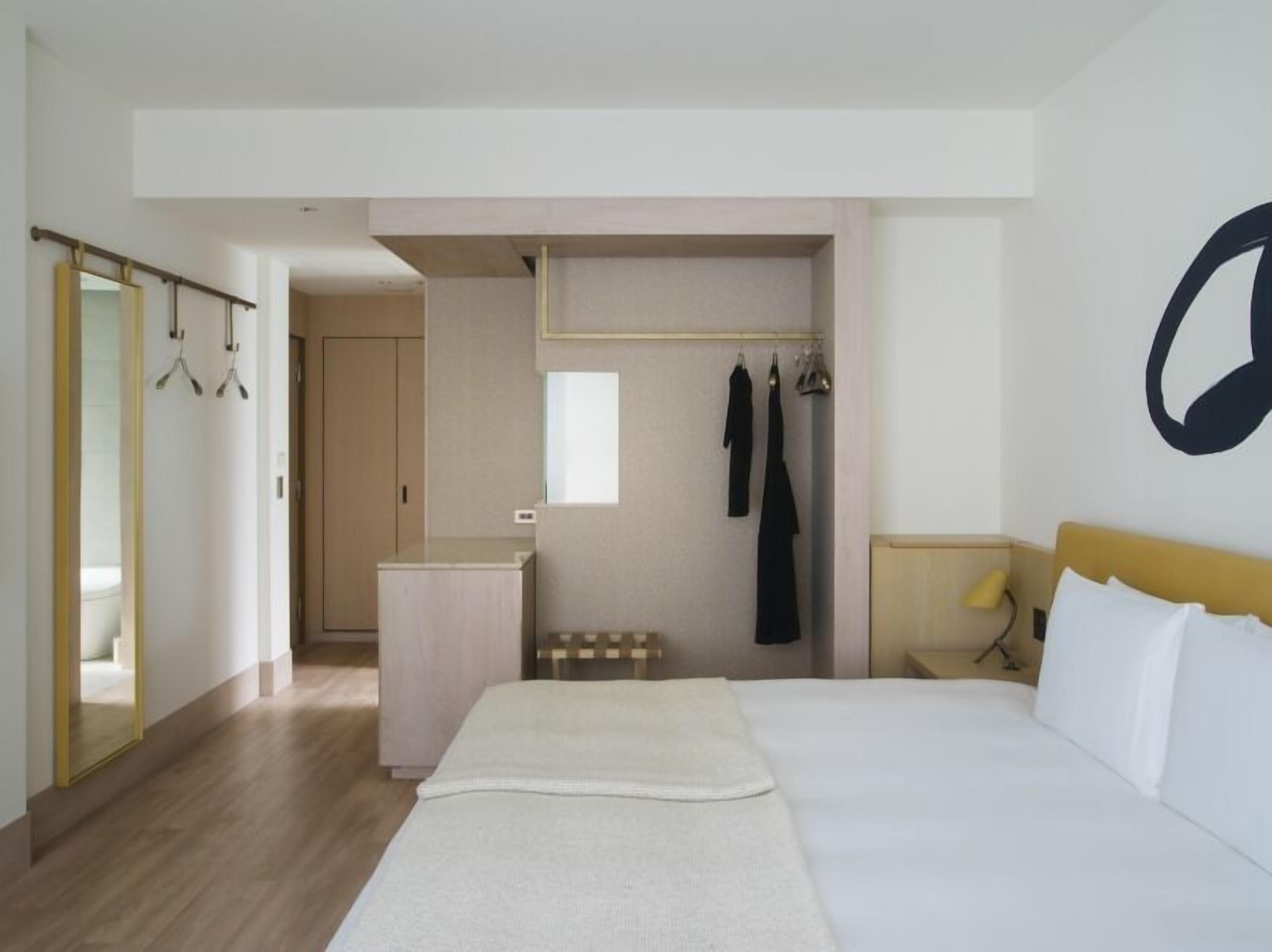 A hotel room with a bed, a wardrobe, a mirror, and a coat rack.