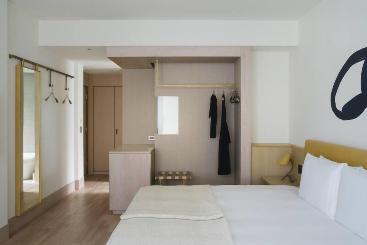 A hotel room with a bed, a wardrobe, a mirror, and a coat rack.