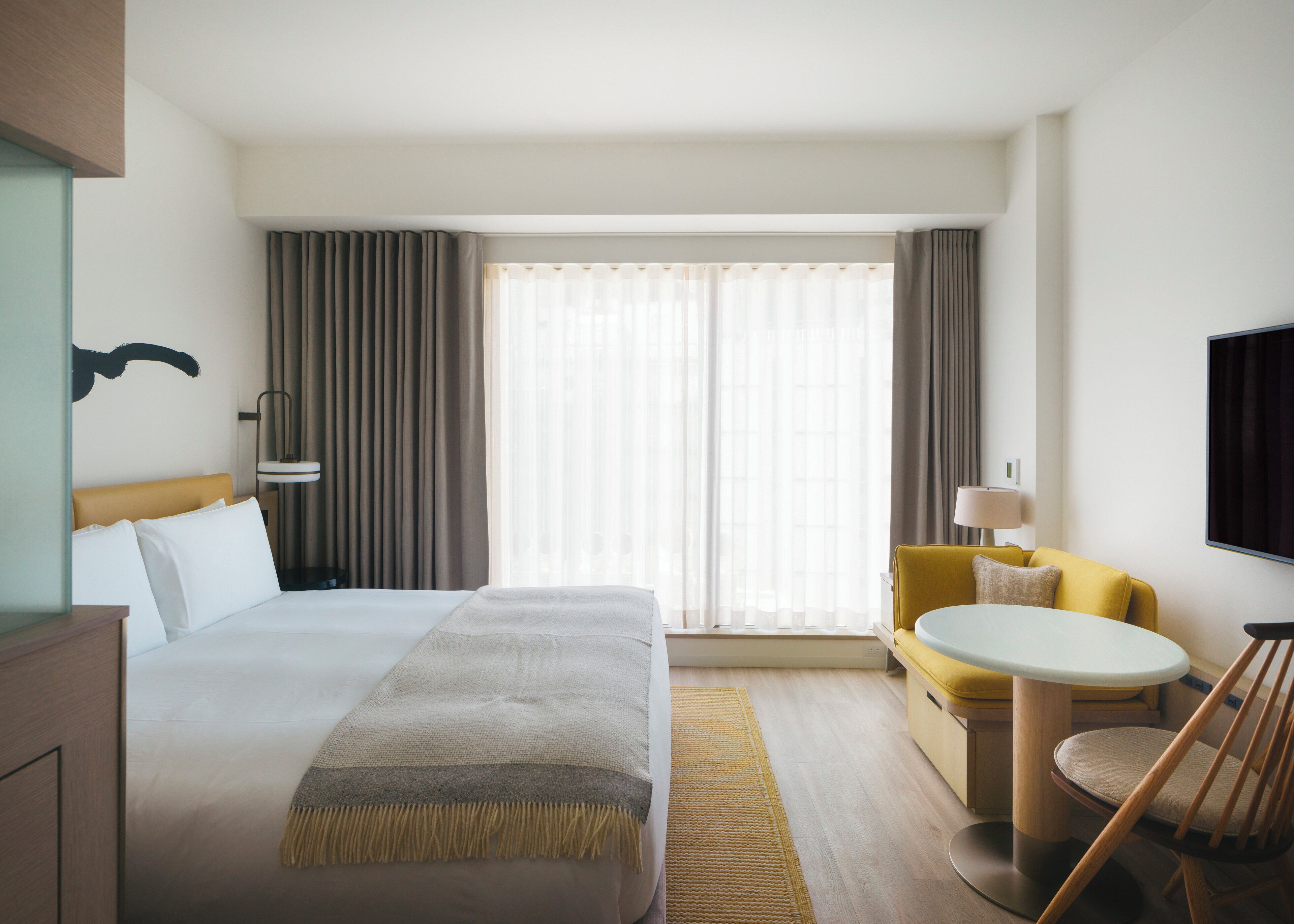A hotel room with a large bed, a desk, a chair, a sofa, and a TV.