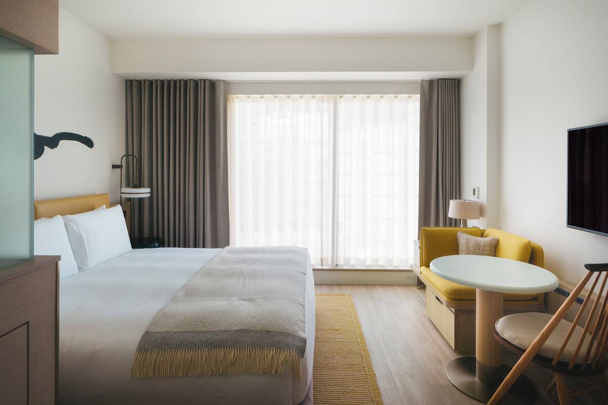 A hotel room with a large bed, a desk, a chair, a sofa, and a TV.