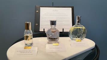 Três frascos de perfume sobre uma mesa de exposição com etiquetas em língua estrangeira, um menu ao fundo e uma parede azul escura.