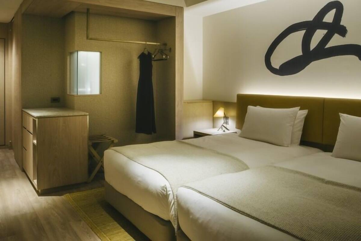 A hotel room with a bed, bedside table, lamp, wardrobe, and a large abstract wall art piece.