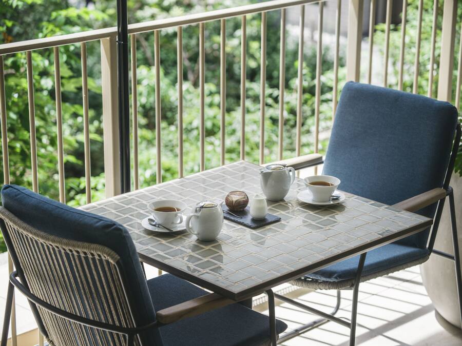 Een balkon met een tafel gedekt voor thee, stoelen en uitzicht op groen.