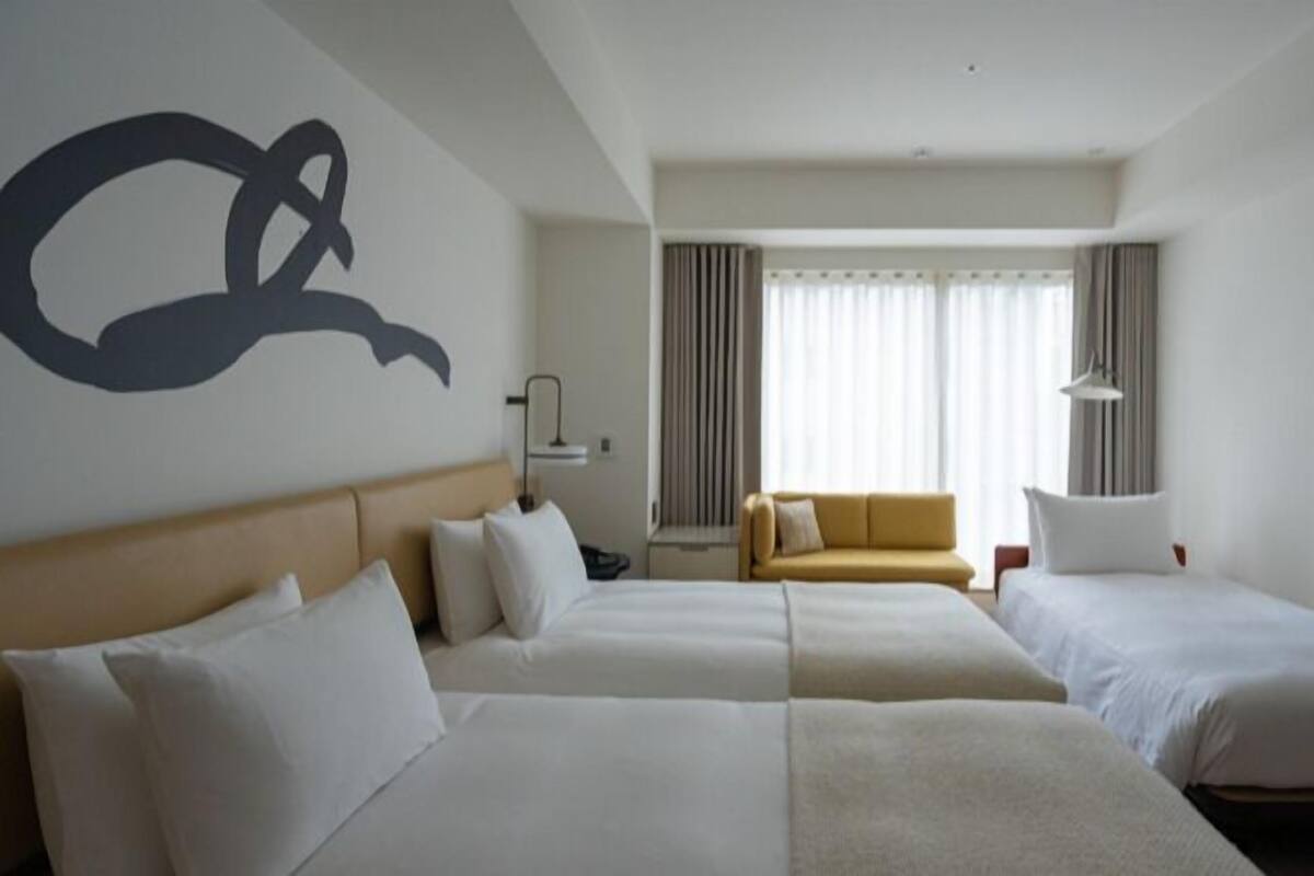 A hotel room with two beds, a sofa, a TV, and a large abstract wall art piece.