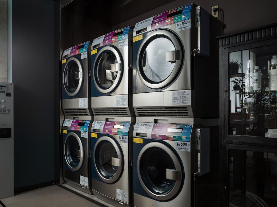 Une rangée de quatre machines à laver à chargement frontal, empilées les unes sur les autres, avec leurs étiquettes de prix et leurs instructions.