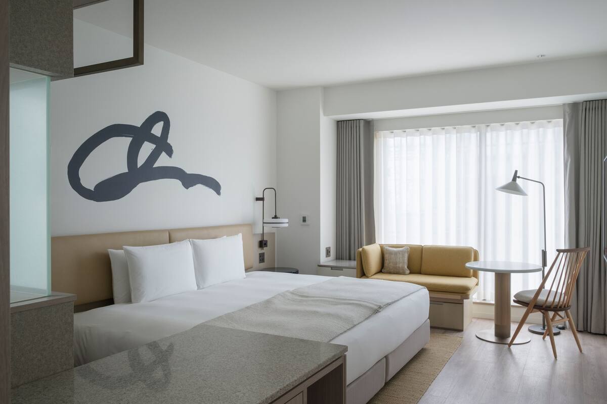 A modern hotel room with a large bed, a sofa, a small table, and a chair.