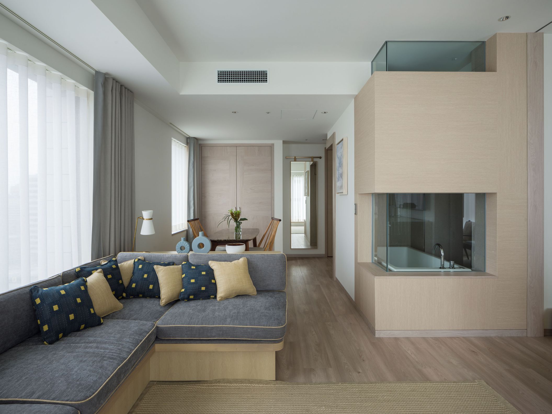 A modern living room with a sectional sofa, a dining area, and a glass-enclosed balcony.