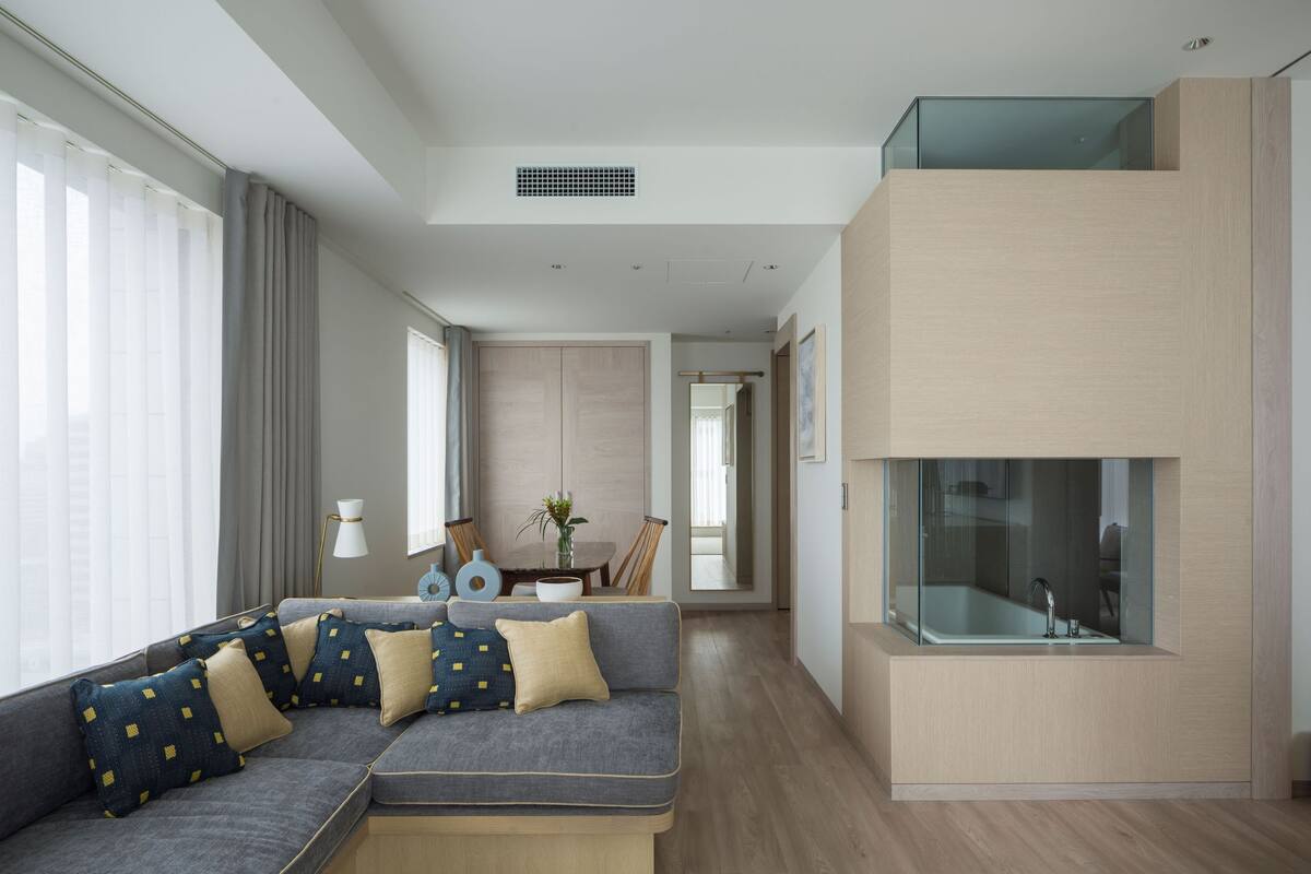A modern living room with a sectional sofa, a dining area, and a glass-enclosed balcony.