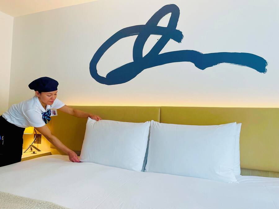 A hotel room with a large bed, a headboard, and a wall with a large abstract painting.