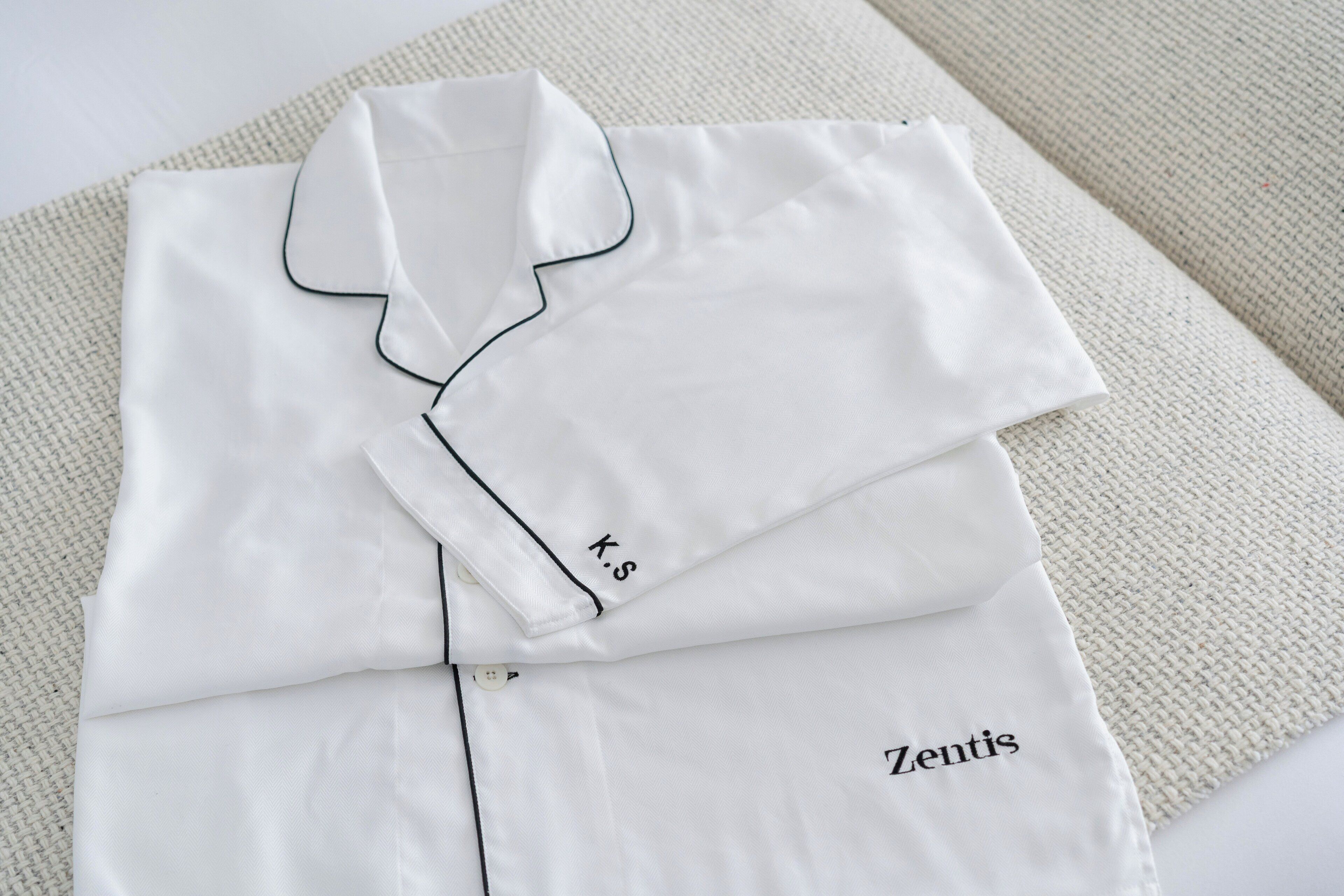 Uma camisa branca bem dobrada com a inscrição 'Zentis' bordada, apoiada em uma superfície texturizada.