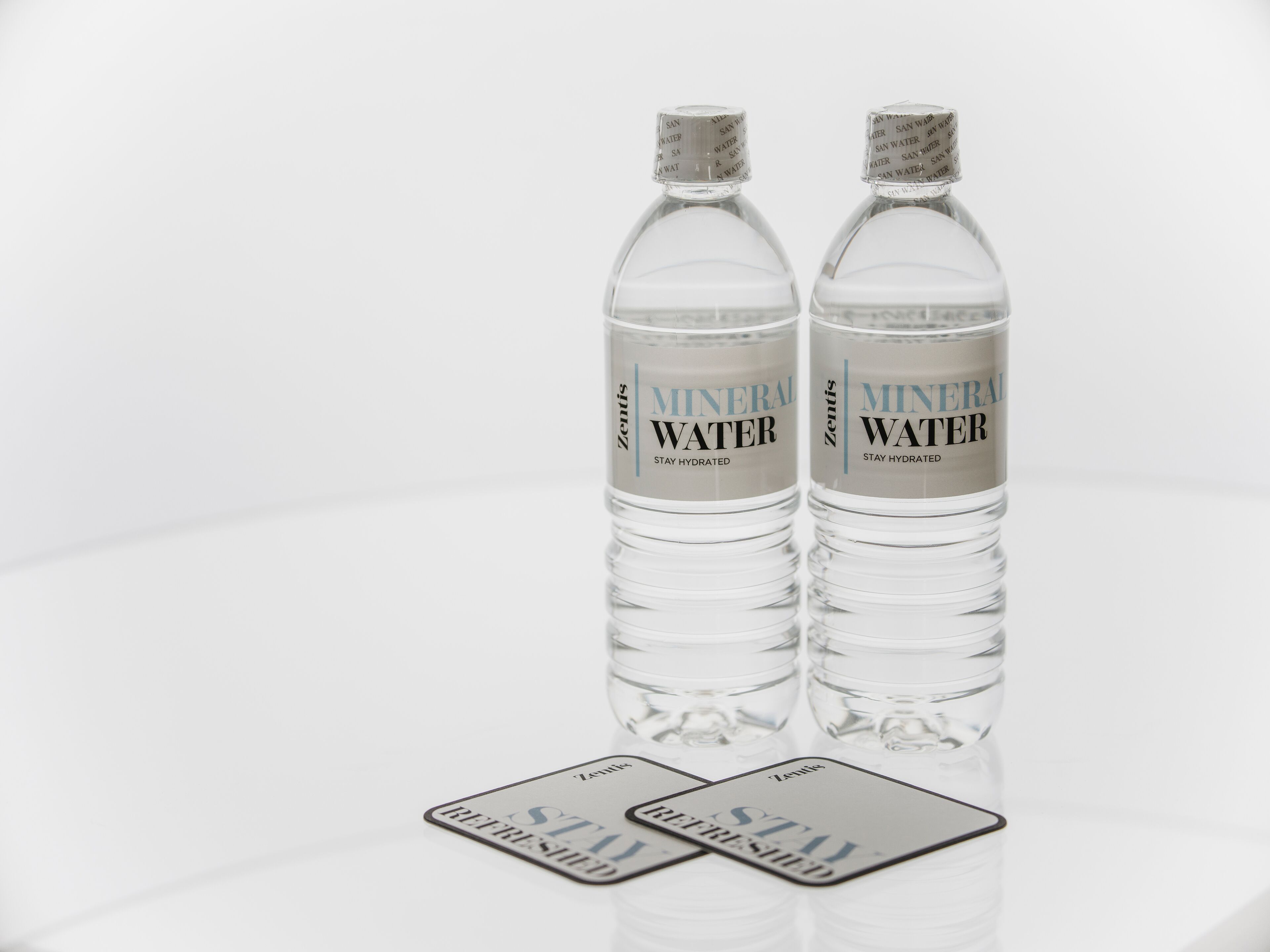 Dos botellas de agua mineral transparente con etiquetas y una tarjeta sobre una superficie reflectante.