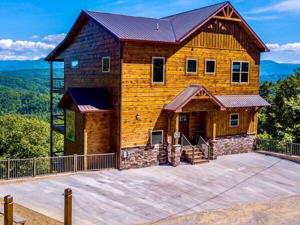 A two-story wooden cabin with a stone foundation, a covered porch, and a concrete driveway.