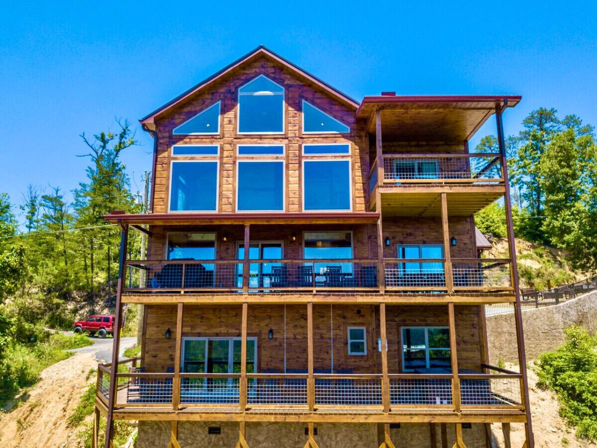 A multi-story wooden cabin with a balcony on the upper floor, surrounded by trees and a dirt path.