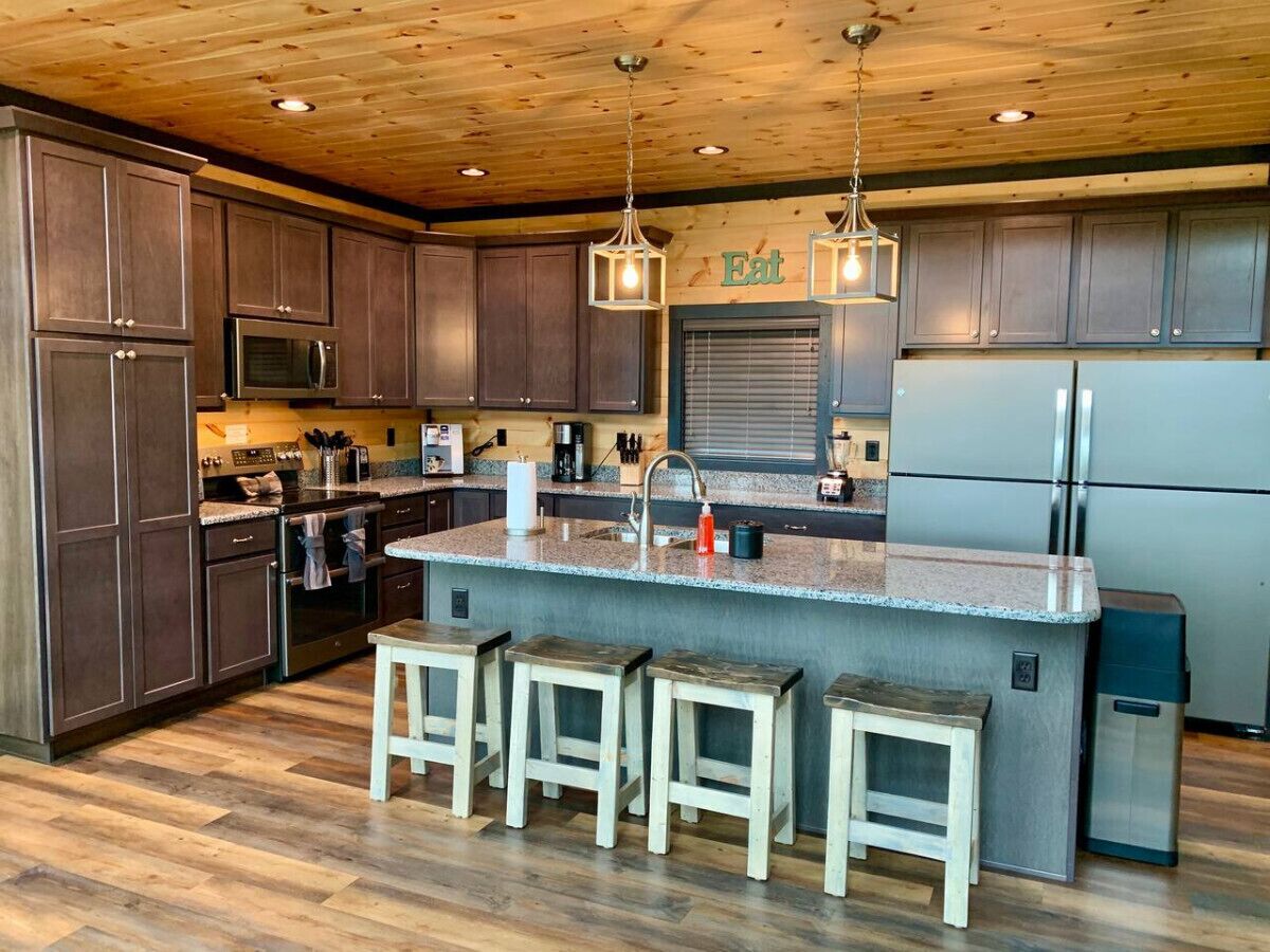 A modern kitchen with dark wood cabinets, a granite countertop, a stainless steel refrigerator, and a wooden ceiling.