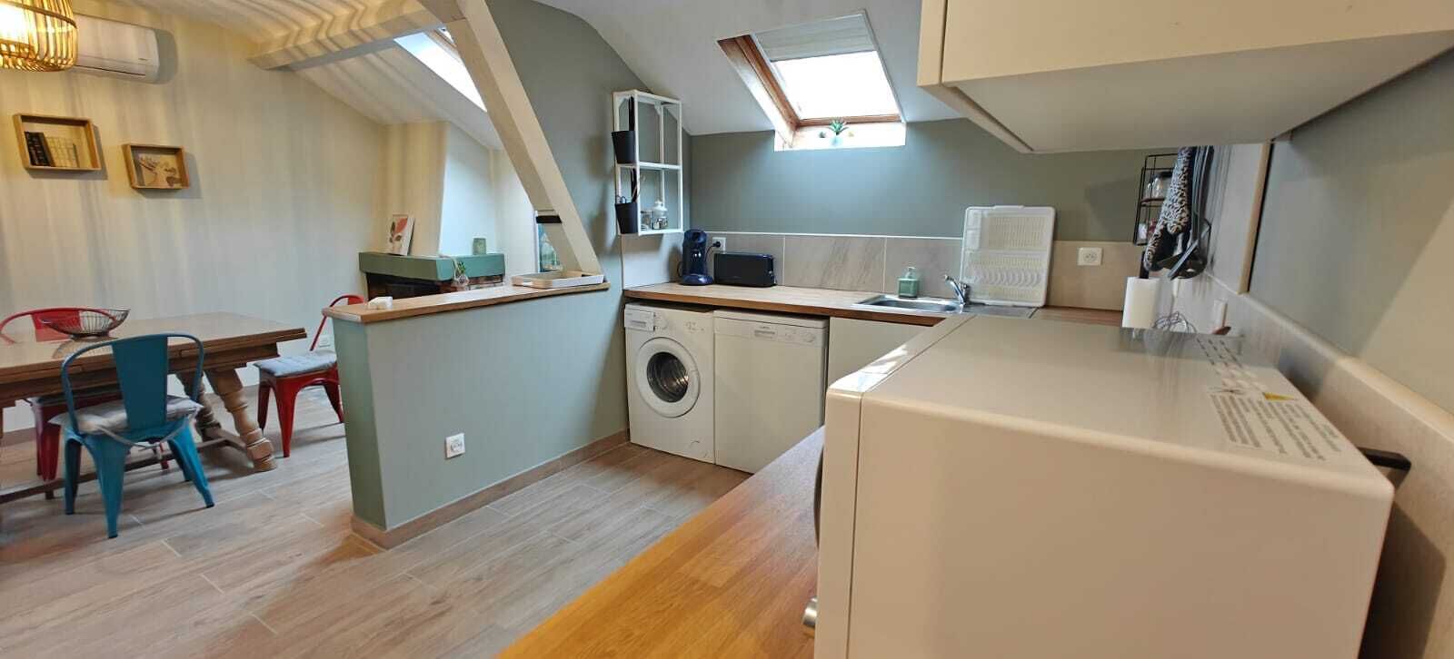 A compact kitchen with a washing machine, a dining area with mismatched chairs, and a small island with a sink.