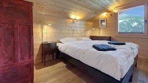 A wooden cabin bedroom with a bed, bedside lamps, a window with a mountain view, and a red door. - Les Granges de Sarreyer - 10 mns from Verbier - Sw (Sarreyer)