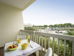 A balcony with a table set for breakfast, a view of a parking area, and a building in the background. - Le Grand Pavois by Interhome (Port Camargue)