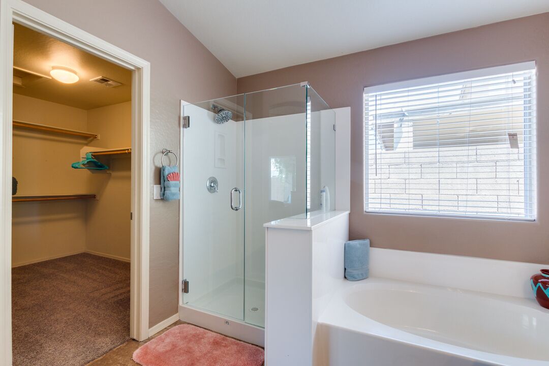 Une salle de bain avec une douche en verre, une baignoire blanche et une fenêtre avec des stores.