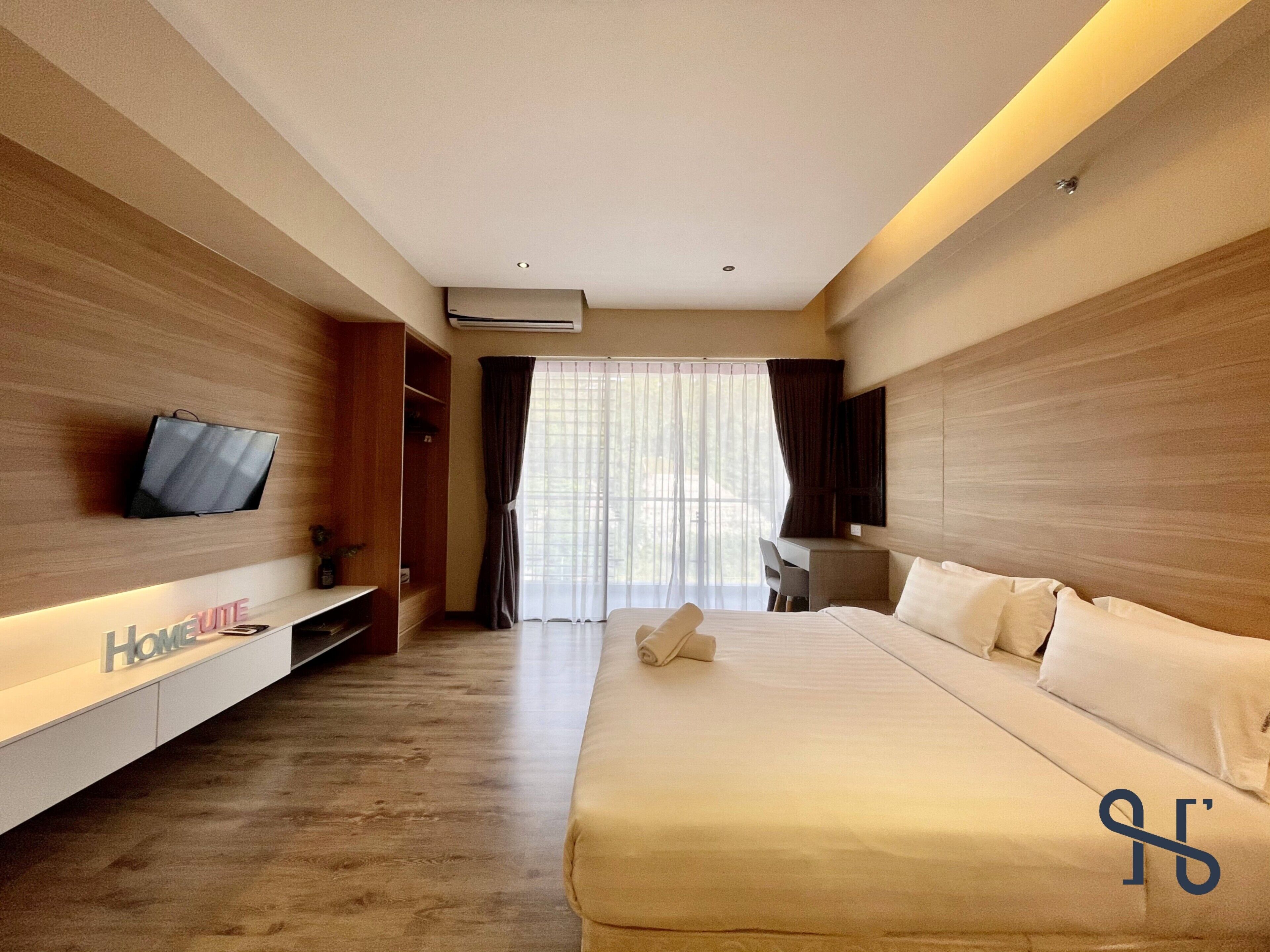 Una habitación de hotel con una cama, un televisor montado en la pared, un escritorio y un armario.