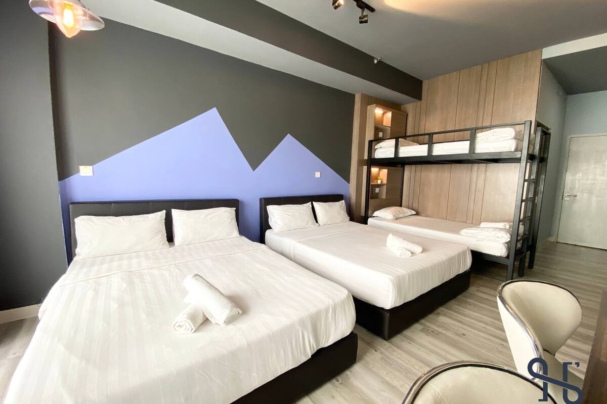 Une chambre d’hôtel avec deux lits, un lit superposé, une chaise et un bureau.