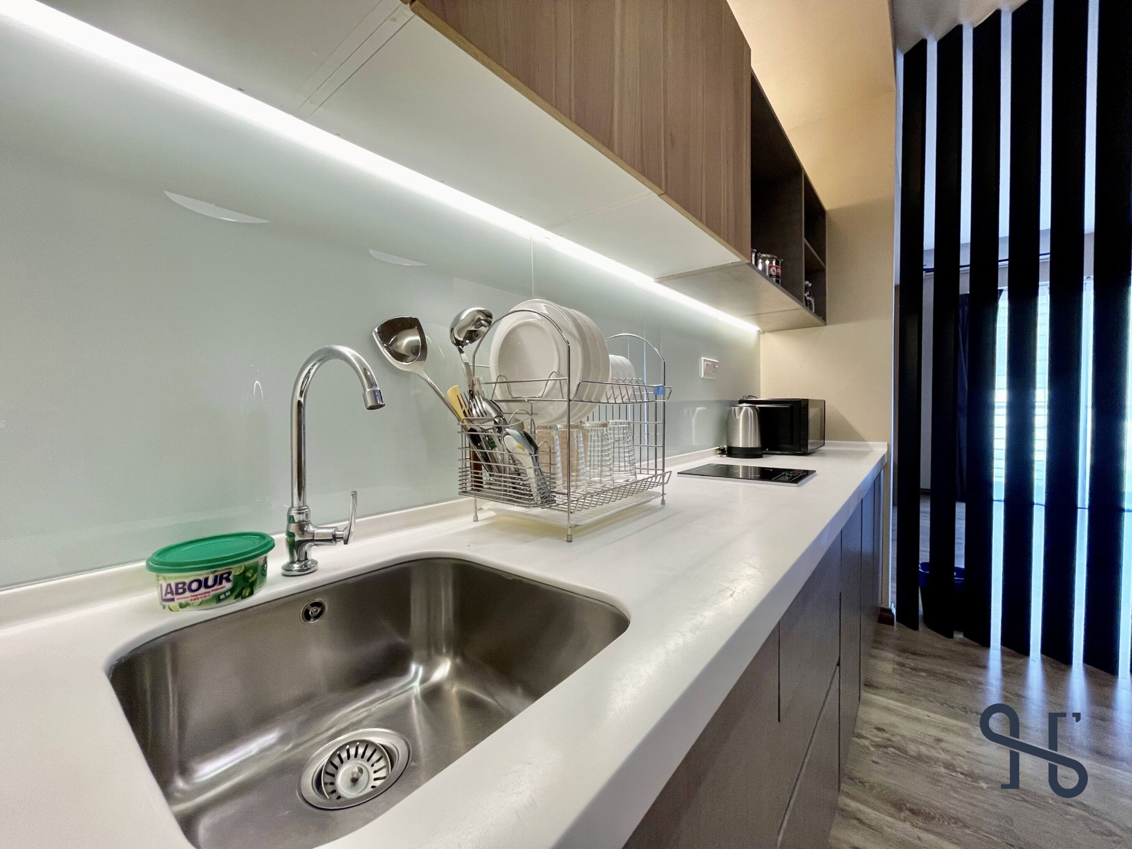 A modern kitchen with a stainless steel sink, a dish rack, and a kettle on the counter.