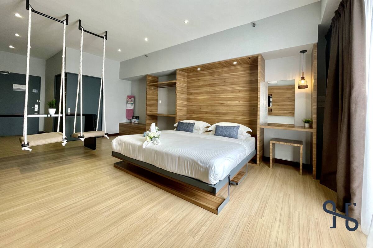 Une chambre moderne avec un grand lit, une tête de lit en bois et un fauteuil suspendu.