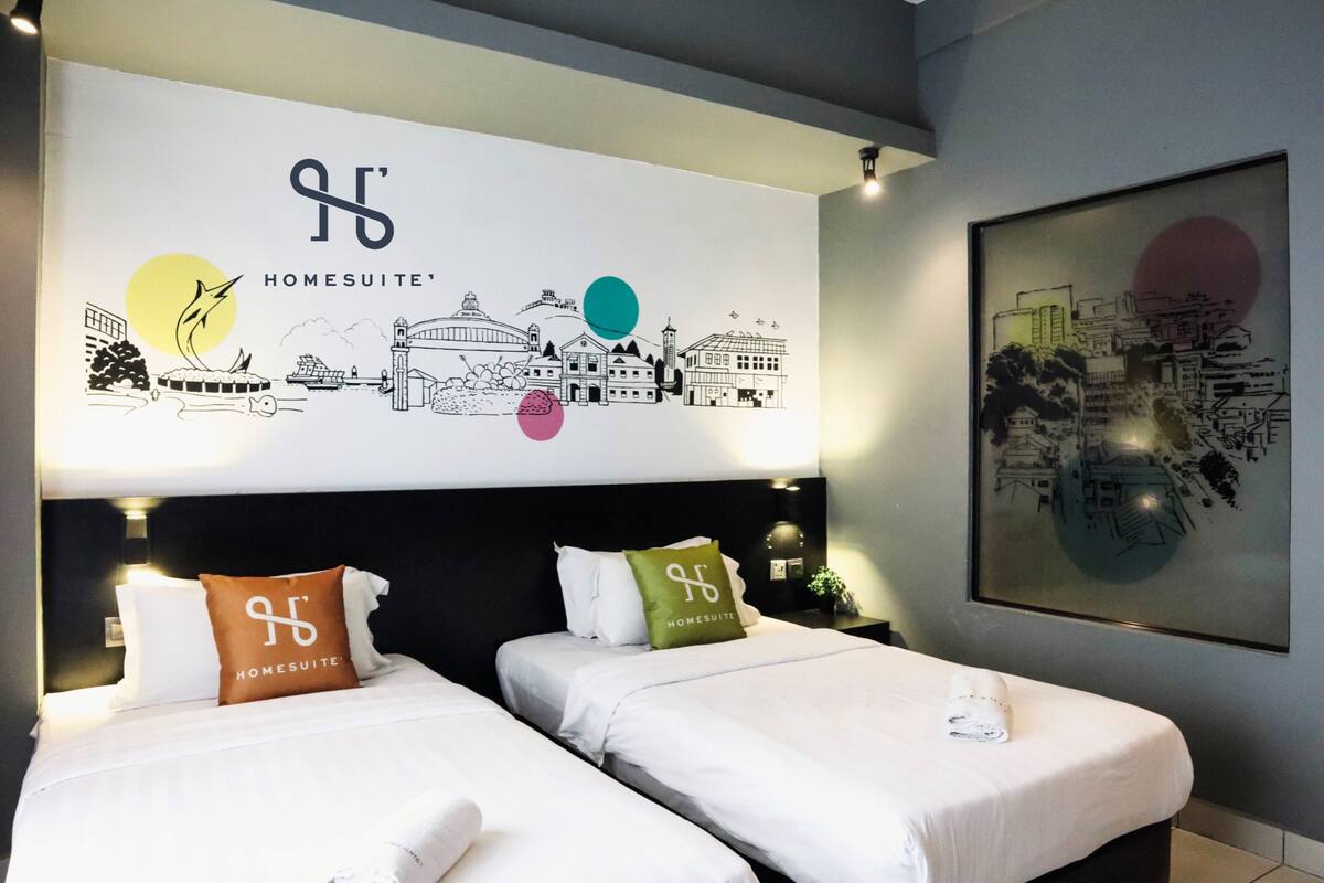 Une chambre d’hôtel avec deux lits, chacun agrémenté de draps et d’oreillers blancs ornés du logo de l’hôtel. Une grande œuvre d’art murale représentant un paysage urbain est visible au-dessus des lits.