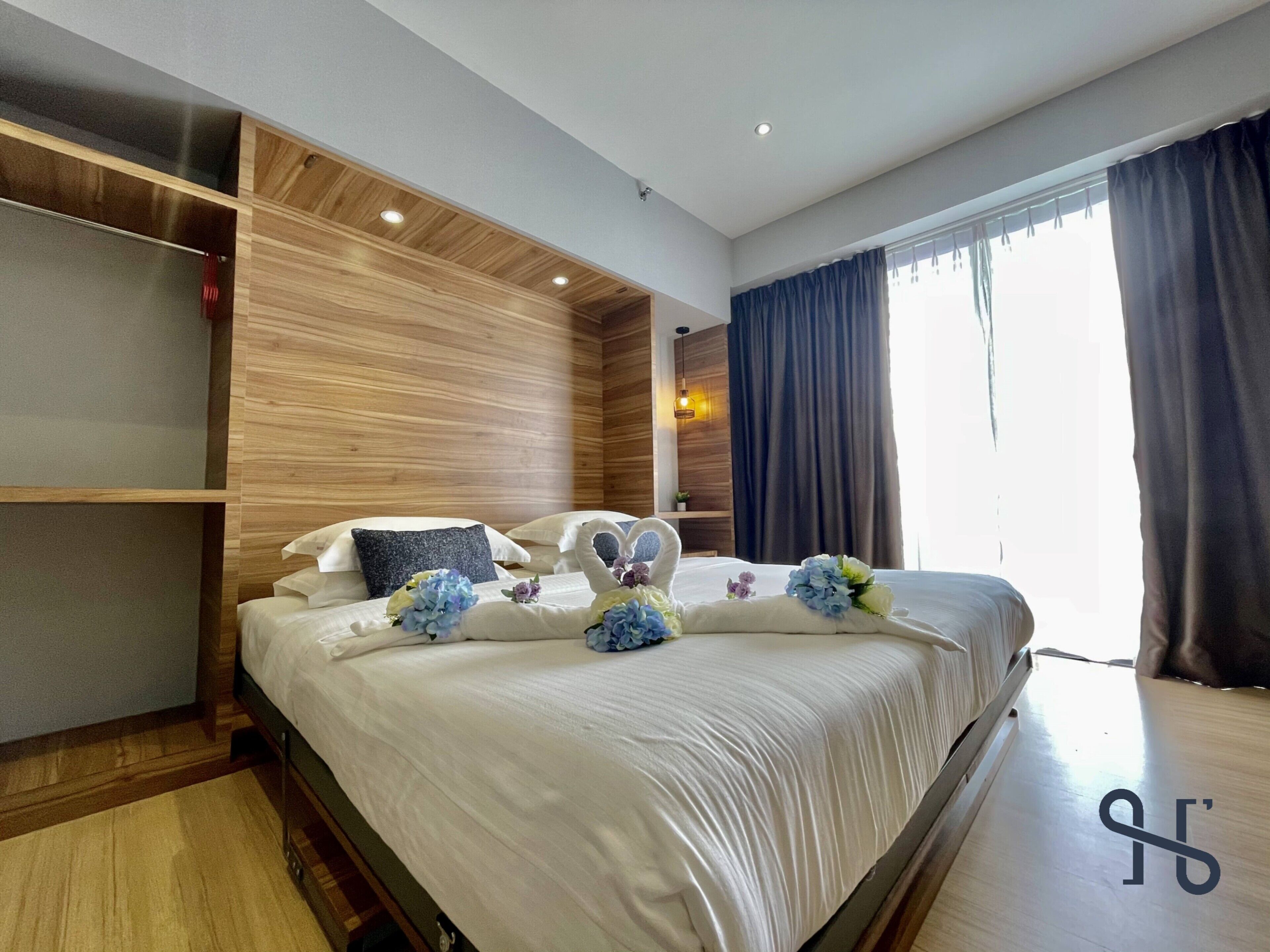 Une chambre d’hôtel moderne dotée d’un grand lit, de lambris en bois, d’une armoire intégrée et d’une grande fenêtre avec des rideaux.