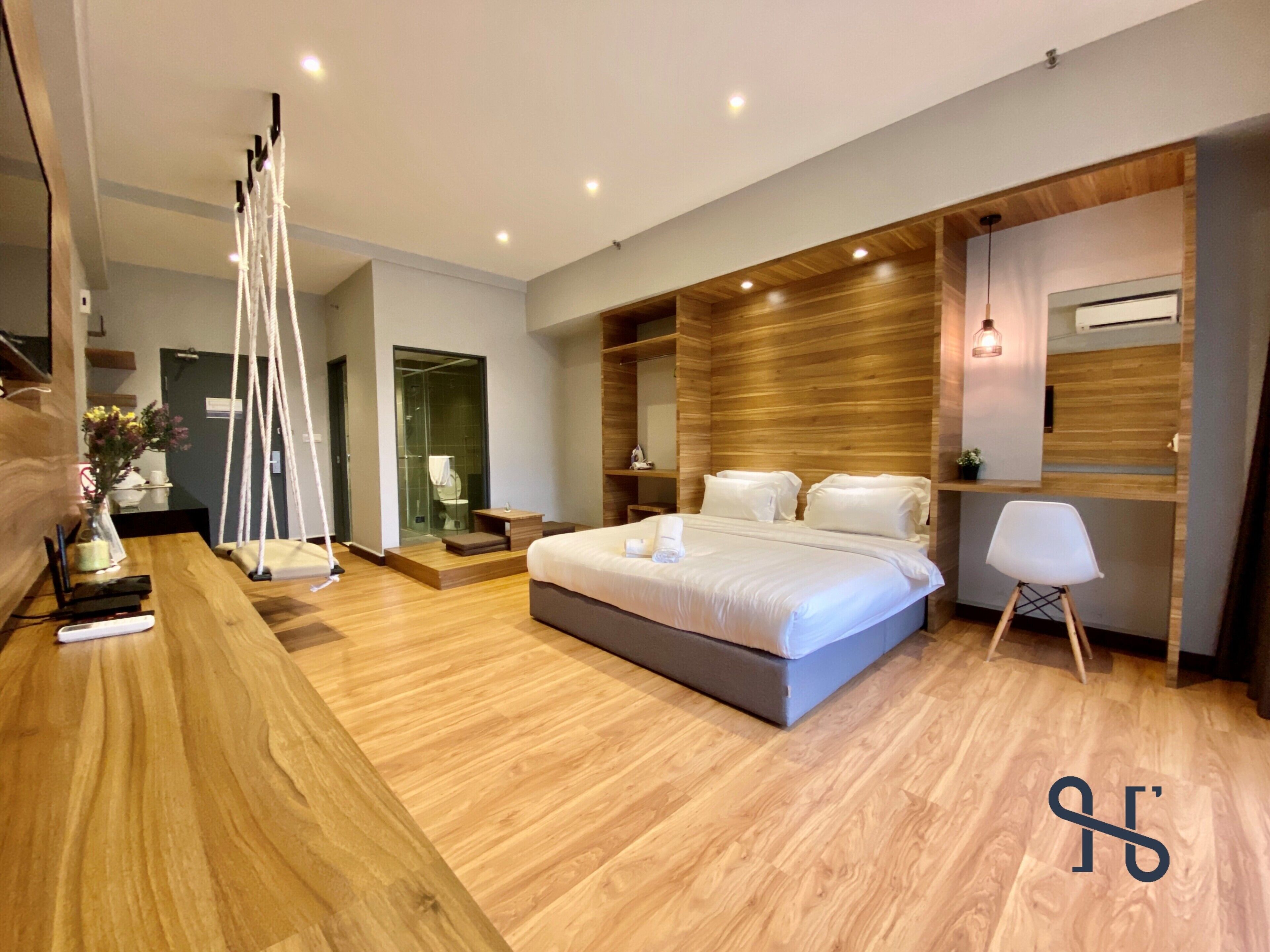 A modern bedroom with a large bed, wooden flooring, a hanging chair, and a glass shower enclosure.