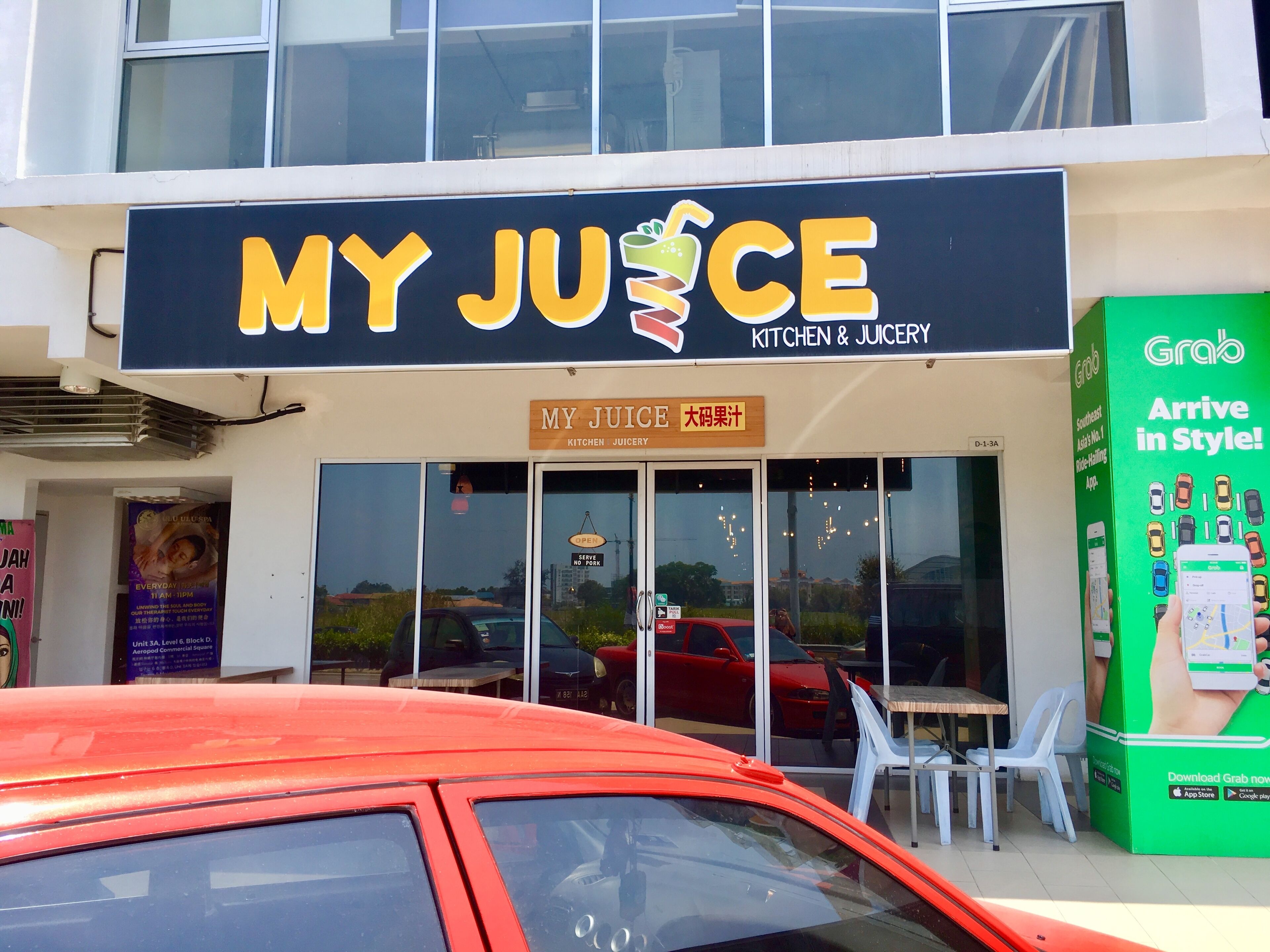 Liiketila, jonka edessä on kyltti, jossa lukee ”MY JUICE KITCHEN & JUICERY”, ja jonka yhteydessä on näkyvillä Grab-ruoan tilaussovelluksen mainos.