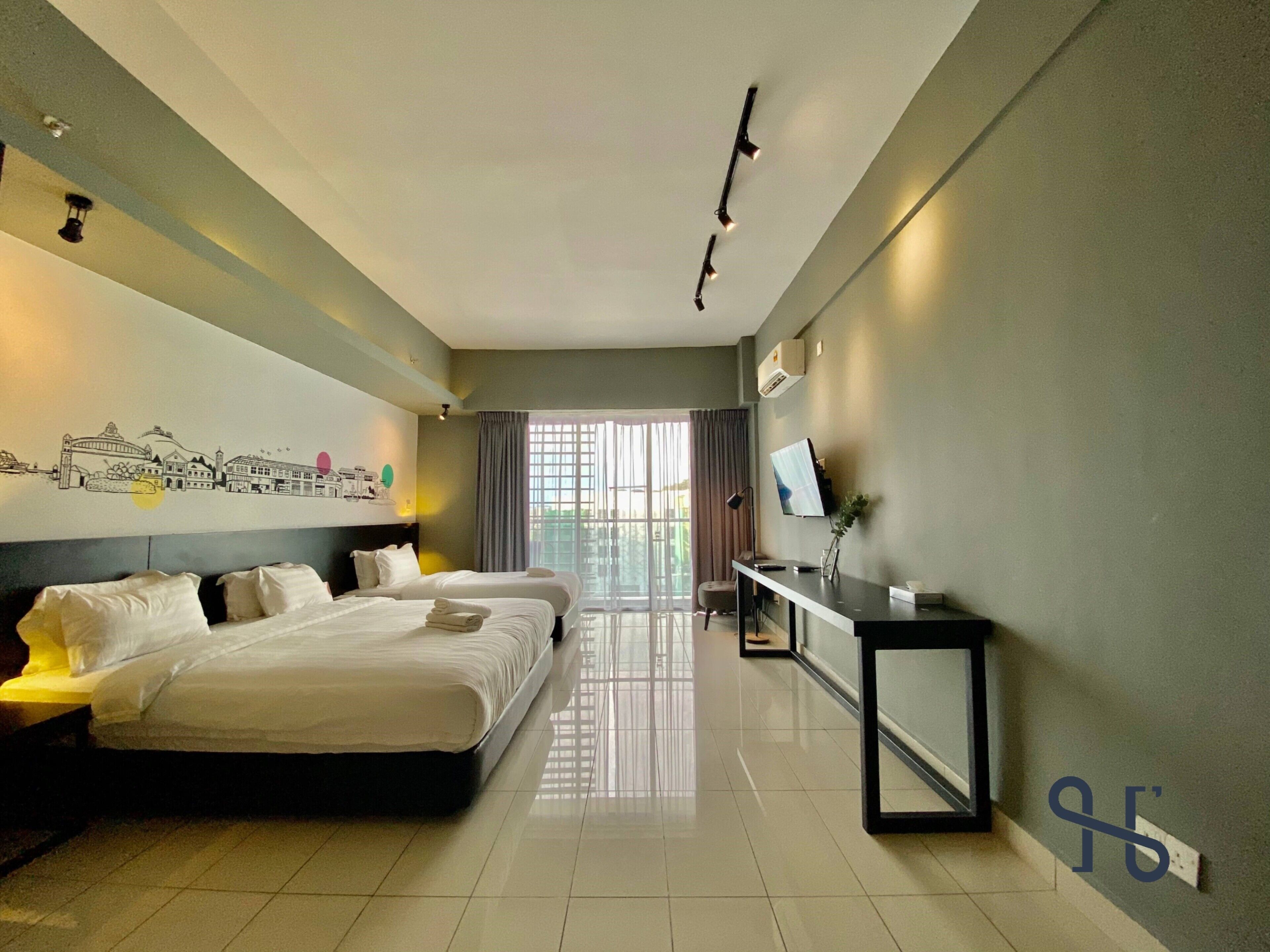 A modern hotel room with two beds, a desk, a TV, and a cityscape mural on the wall.