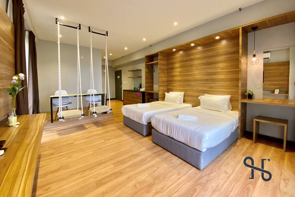 Une chambre d’hôtel moderne avec deux lits, un bureau et un fauteuil suspendu.