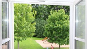 A view through a window of a grassy area with trees and a playground.