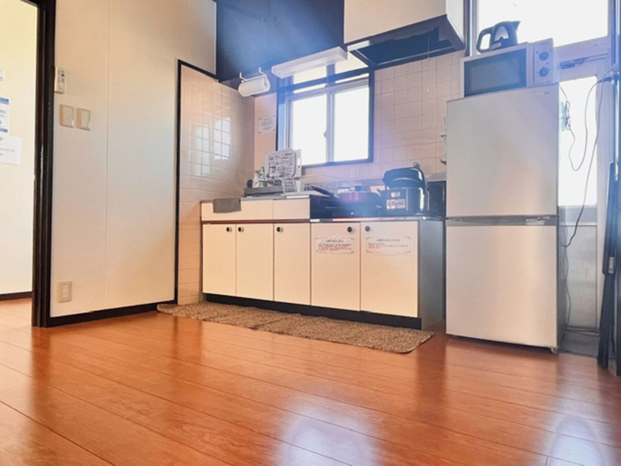 A compact kitchen with wooden flooring, white cabinets, a microwave, and a refrigerator.