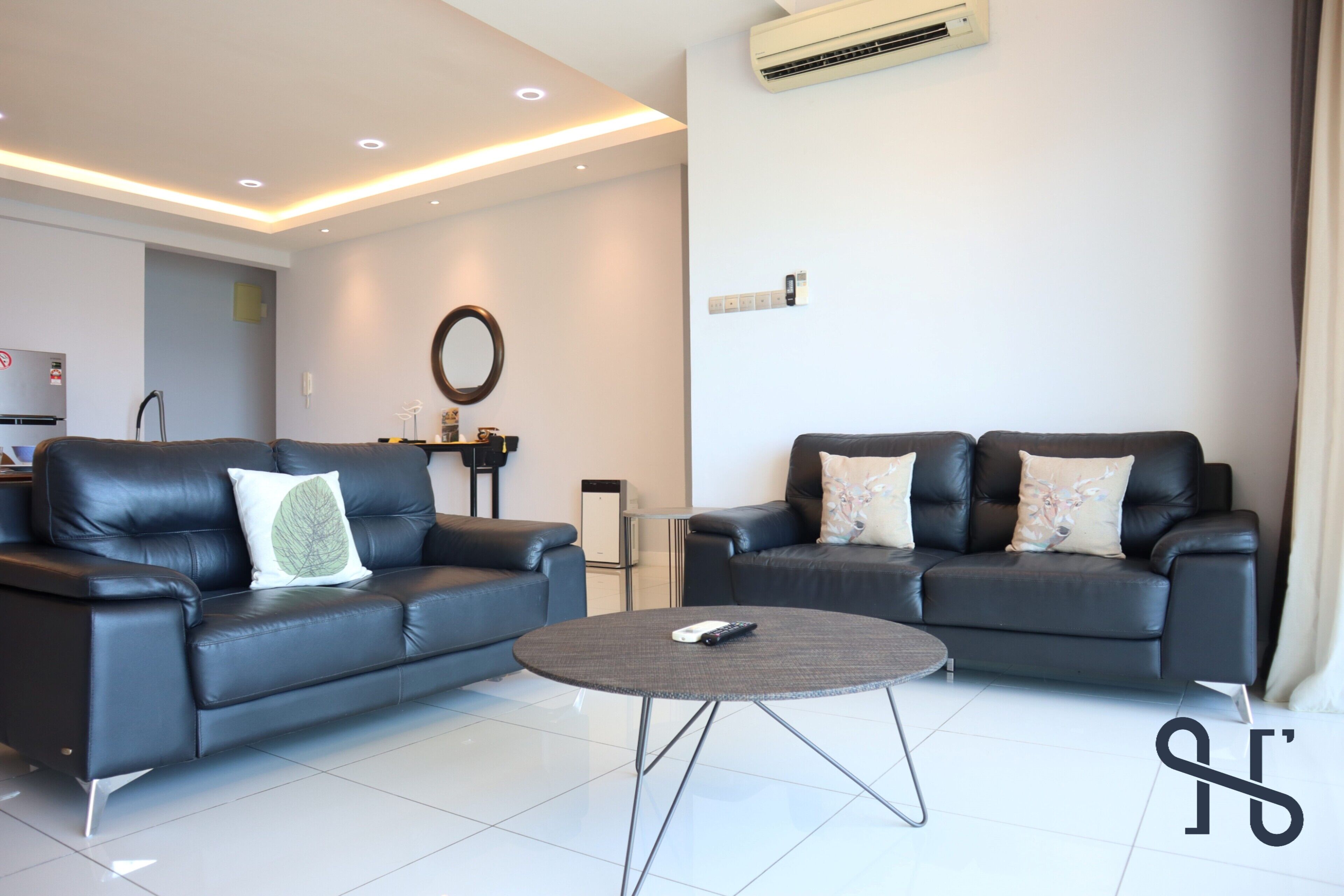 A modern living room with two black leather sofas, a round coffee table, and a wall-mounted air conditioner.