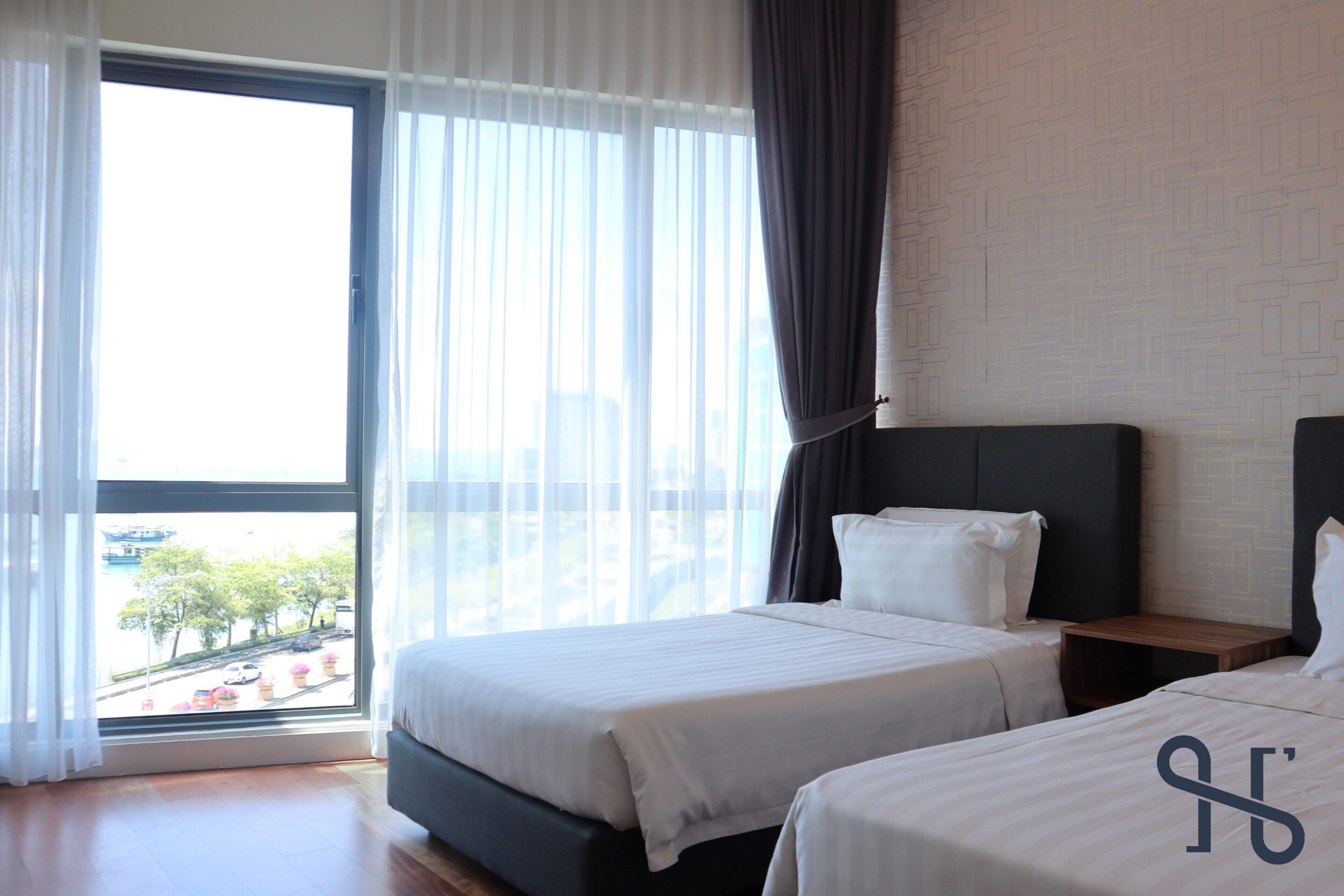 A hotel room with two beds, a large window with curtains, and a view of the cityscape.