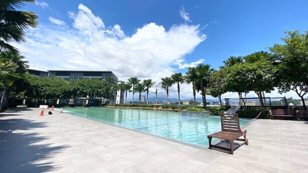 Un espace piscine doté d’une terrasse carrelée, d’un banc en bois et de palmiers.