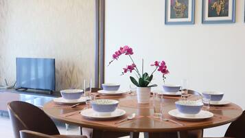 A dining table set with bowls, plates, and cutlery, surrounded by chairs, with a potted plant and framed artwork on the wall.