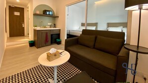 A modern hotel room with a sofa, a small table, a lamp, a kitchenette, and a bed with a view. - Homi Oasis 和逸绿洲 (Kota Kinabalu)