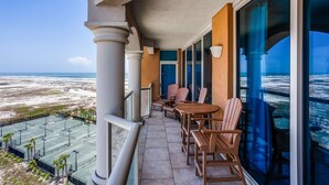 Een balkon met uitzicht op het strand en de oceaan, met een tafel en stoelen, en een glazen deur die naar binnen leidt.