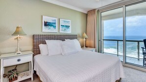 Een hotelkamer met een groot bed, twee nachtkastjes, een plafondventilator en uitzicht op de oceaan.